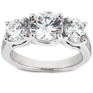 Three-stone diamond ring with a central large round diamond flanked by two smaller round diamonds, set in a polished white metal band.