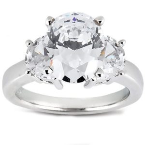 Three-stone engagement ring with a central round diamond flanked by two smaller round diamonds, set on a polished silver band.