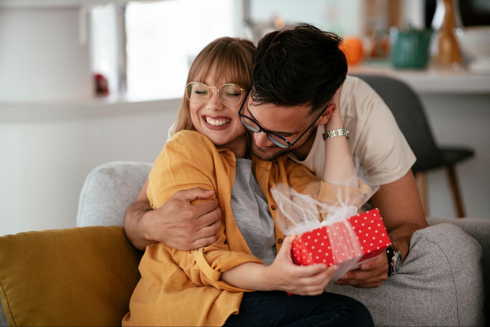 A woman being hugged by her partner while receiving a gift